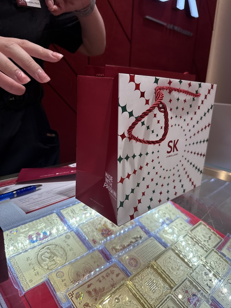 A SK Jewellery shopping bag, gold products, and a staff member's hand are visible in the shop.