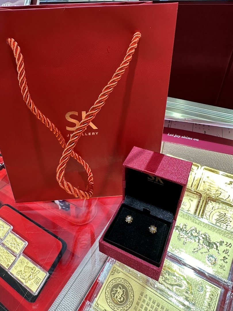 A red SK Jewellery shopping bag, an open jewellery box with earrings, and gold items on display.