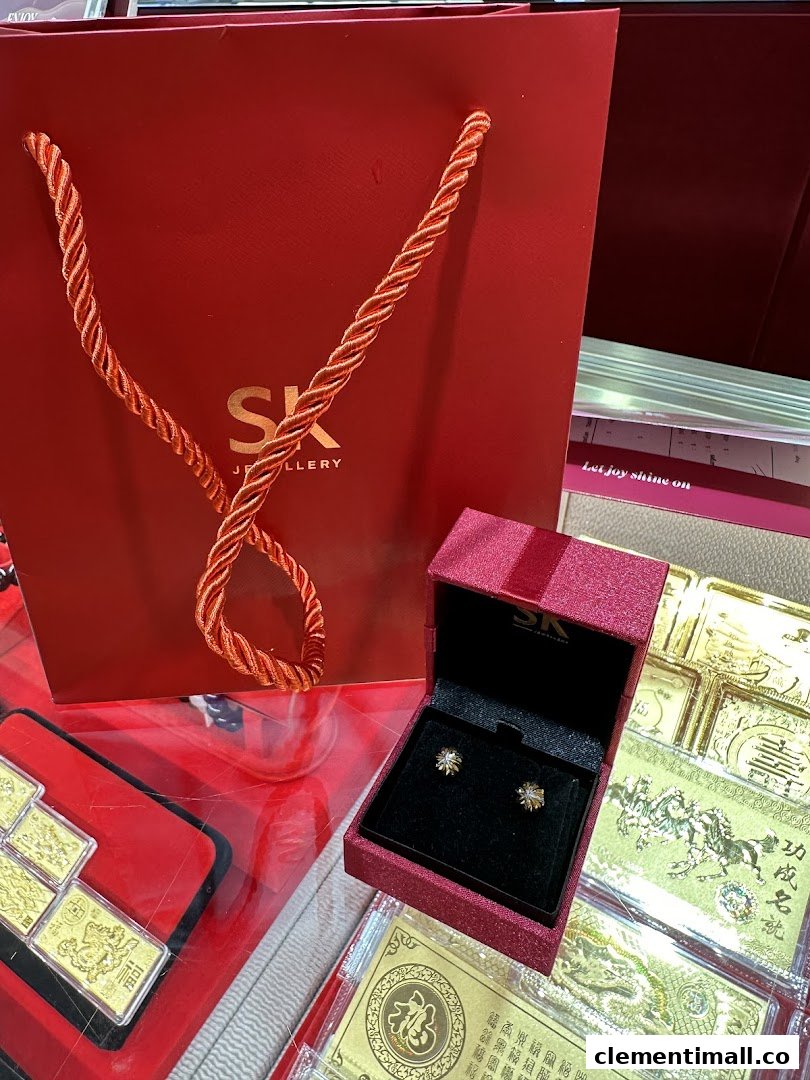 A red SK Jewellery shopping bag, an open jewellery box with earrings, and gold items on display.
