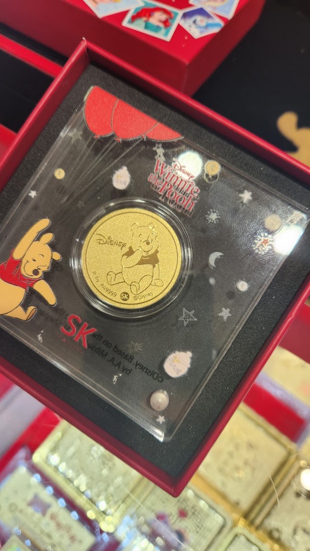 A close-up of a Disney Winnie the Pooh gold coin in its display case from SK Jewellery.