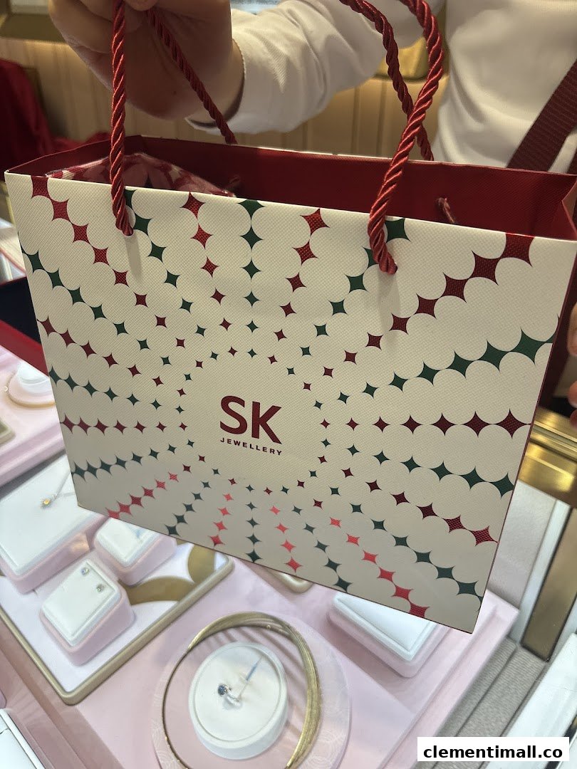 A person holds an SK Jewellery shopping bag, with elegant jewellery displays visible in the background.
