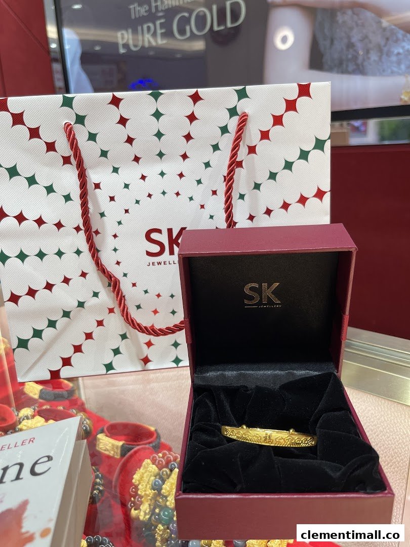 A gold bracelet in an open SK Jewellery box with a branded shopping bag and display.