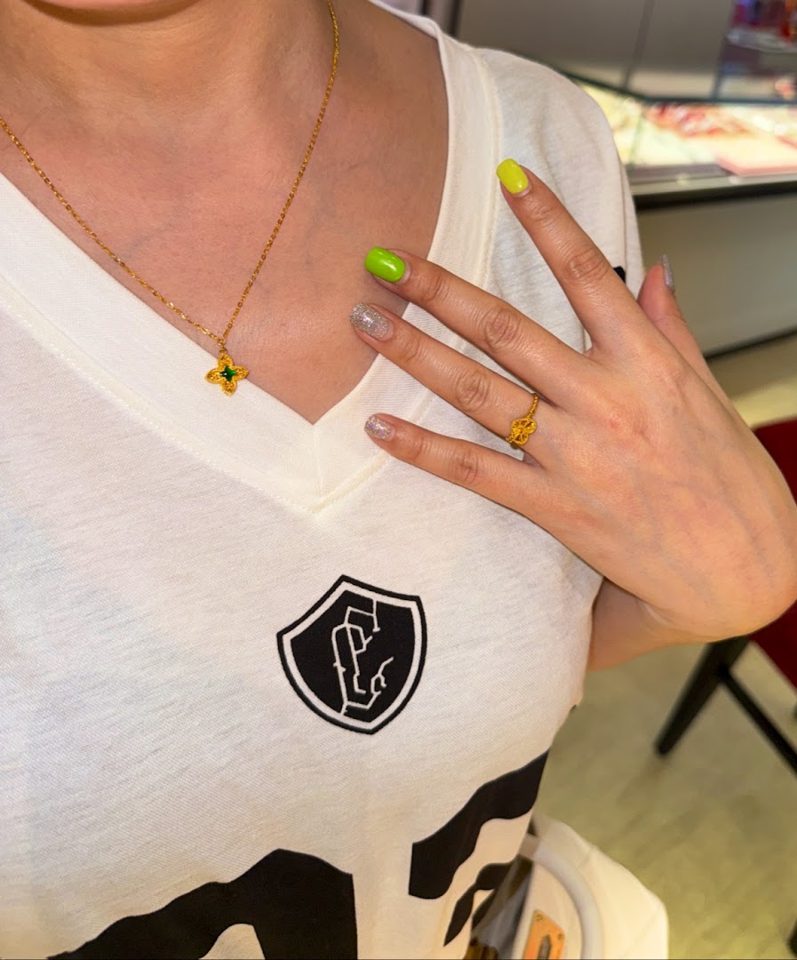 A person showcases a delicate gold necklace with a green pendant and a matching gold ring.