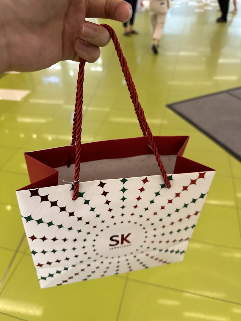 A hand holds a white SK Jewellery shopping bag with red and green star patterns.