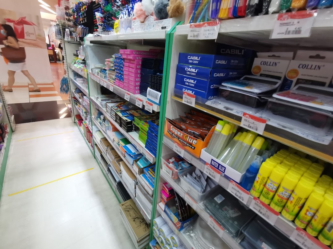 An aisle in a stationery shop displaying various office supplies, glues, and calculators on shelves.