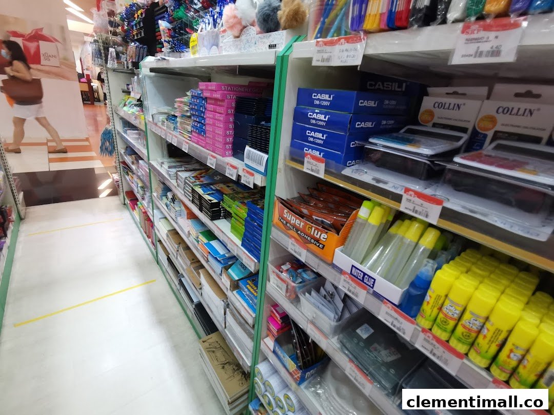 An aisle in a stationery shop displaying various office supplies, glues, and calculators on shelves.