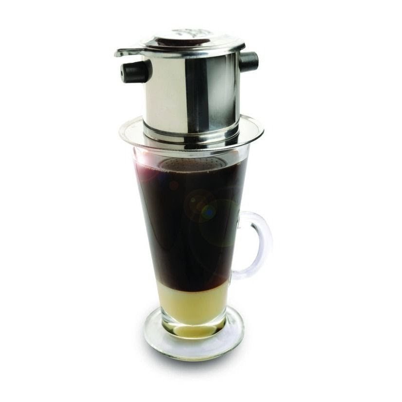 A Vietnamese phin filter brewing coffee into a glass with condensed milk.