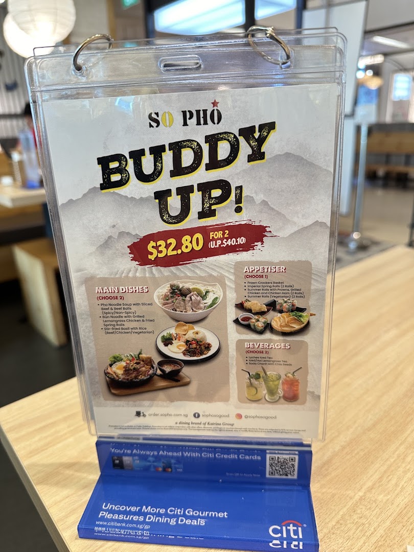 A promotional menu stand for So Pho's 'Buddy Up!' meal deal, featuring Vietnamese dishes and drinks.