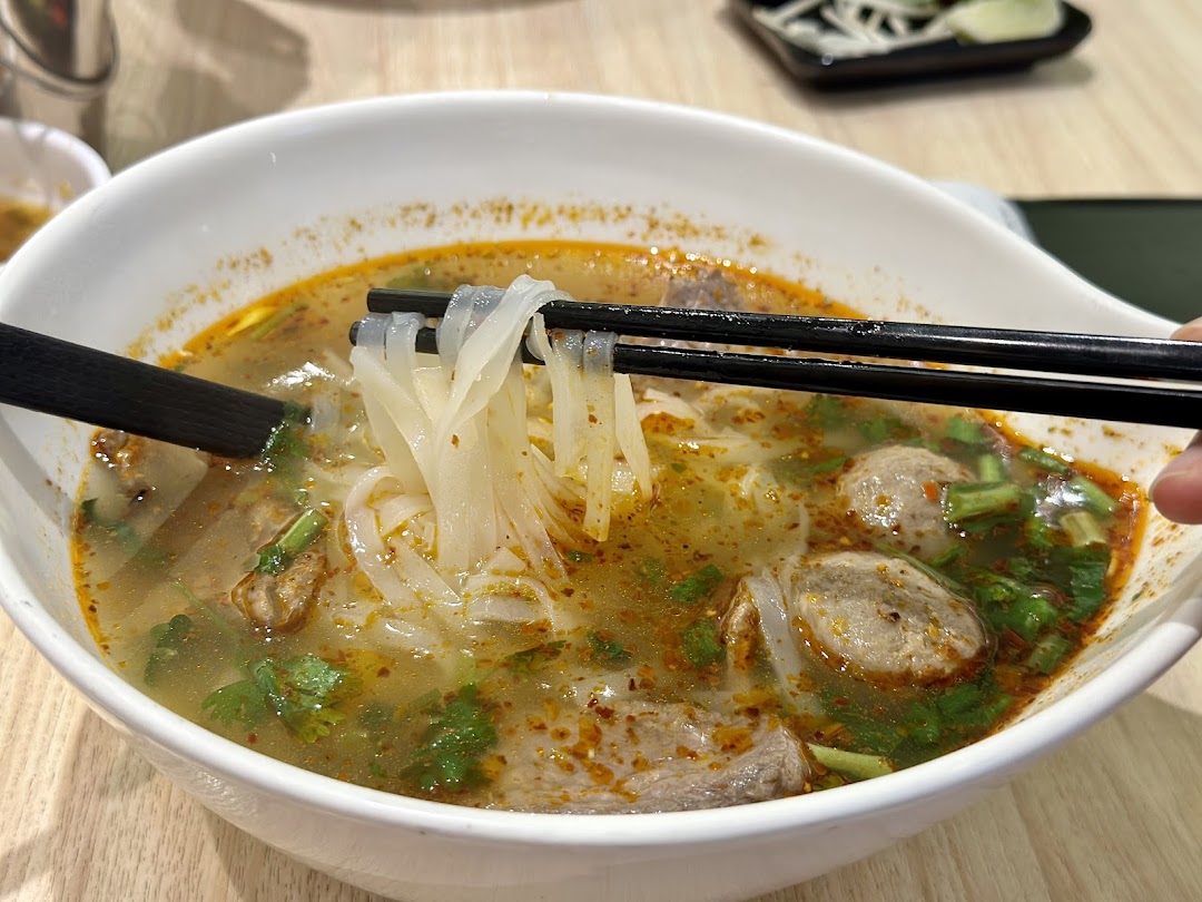 A close-up of a bowl of Vietnamese pho with noodles being lifted by chopsticks.