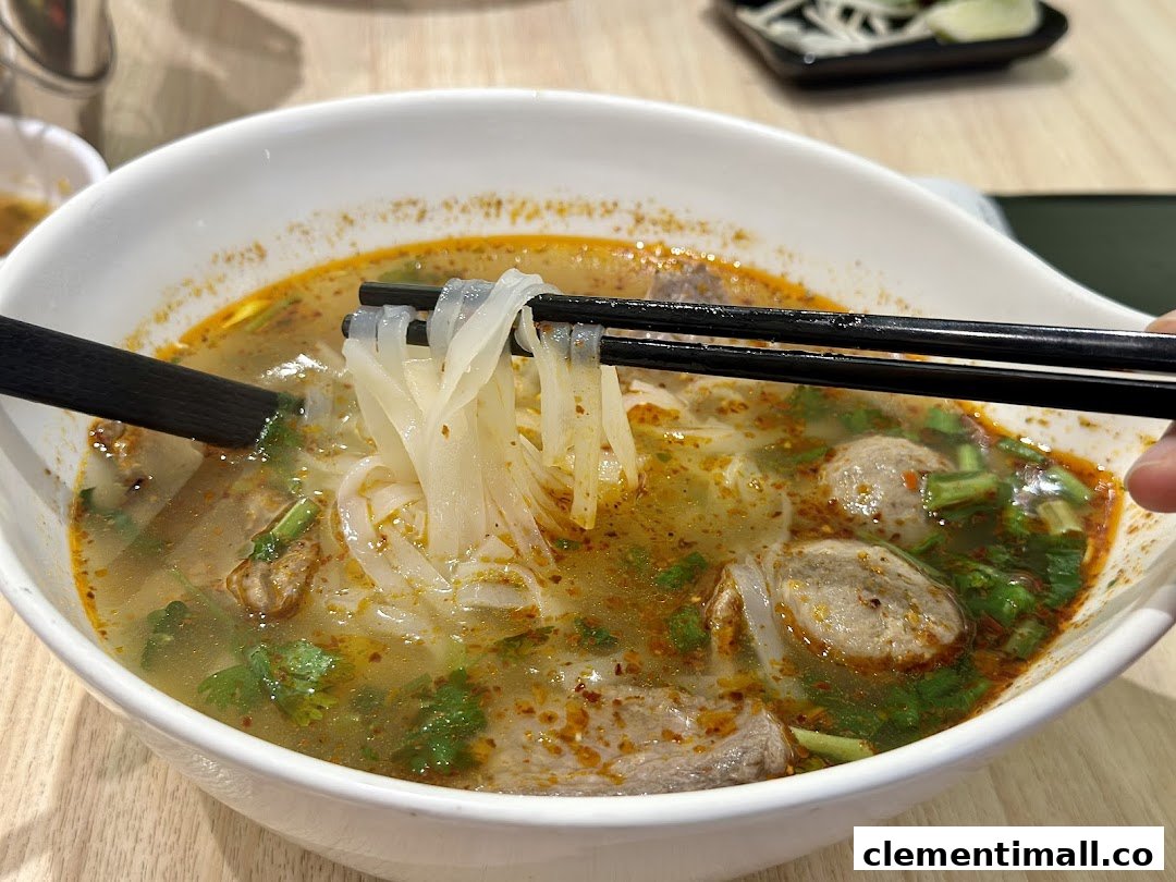 A close-up of a bowl of Vietnamese pho with noodles being lifted by chopsticks.