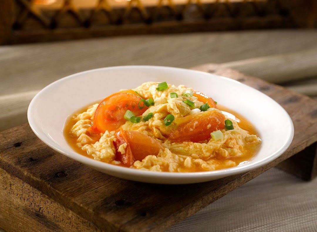 A white bowl filled with scrambled eggs and sliced tomatoes, garnished with green onions.