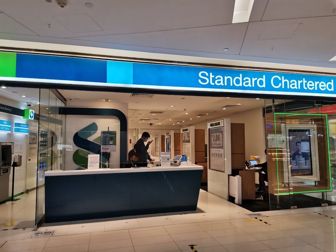 The modern glass facade of a Standard Chartered Bank branch with a customer service counter.