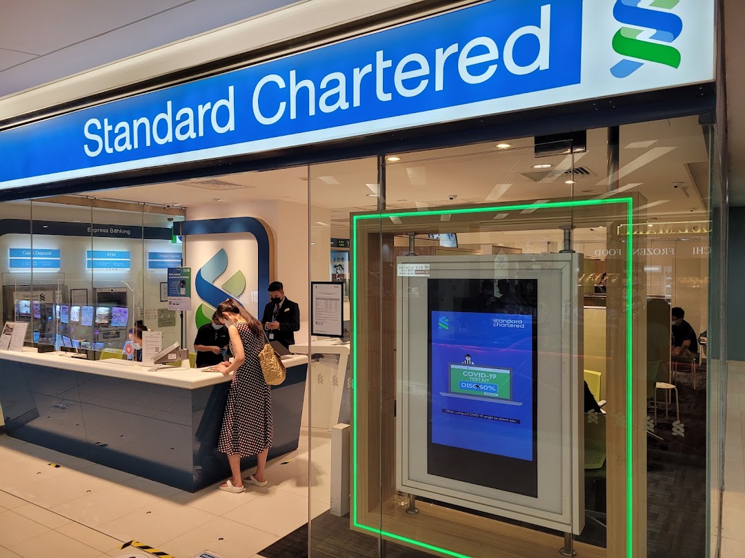 The front entrance of a Standard Chartered Bank branch with customers and staff inside.