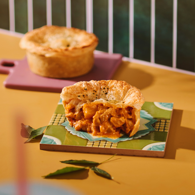 Close-up of a delicious savory pie, cut open to show its rich, flavorful filling, with another pie in the background.