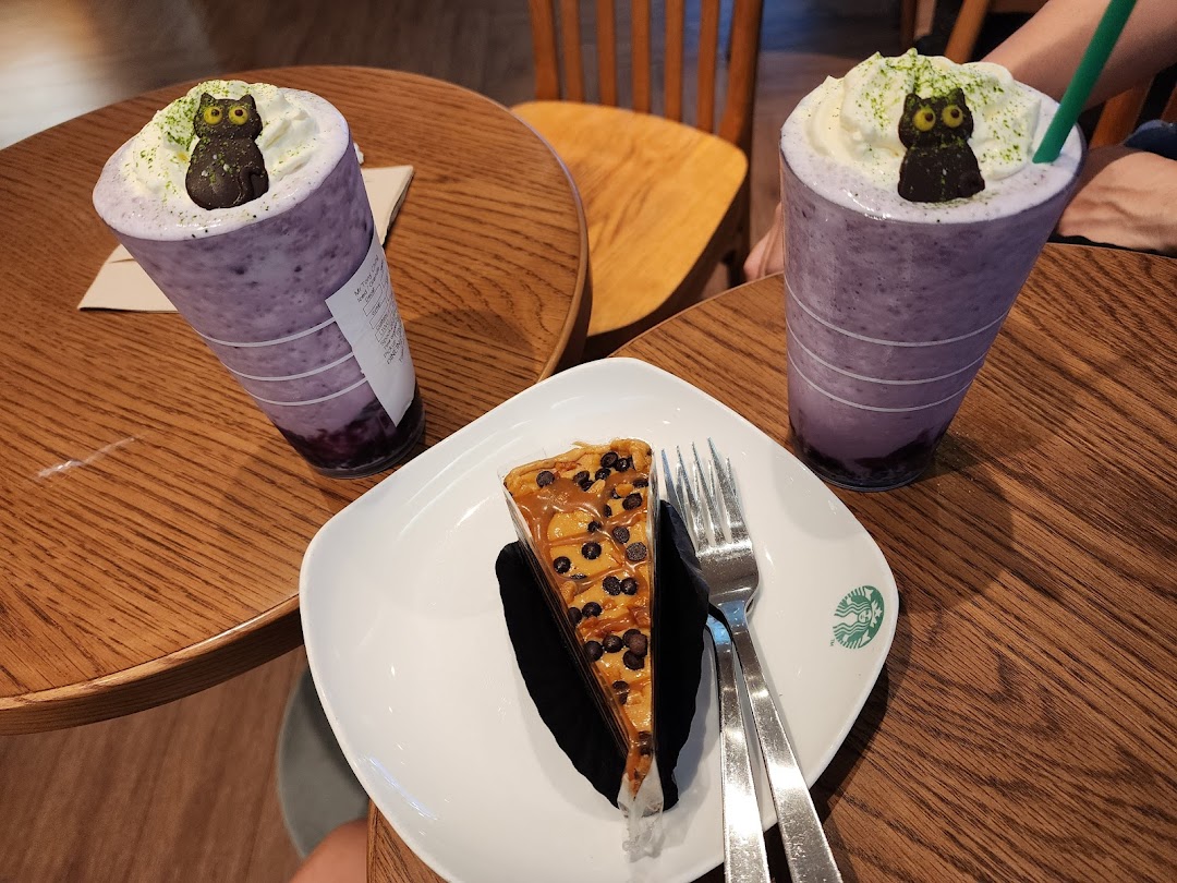 Two purple beverages with whipped cream and owl decorations, alongside a slice of cake on a wooden table.