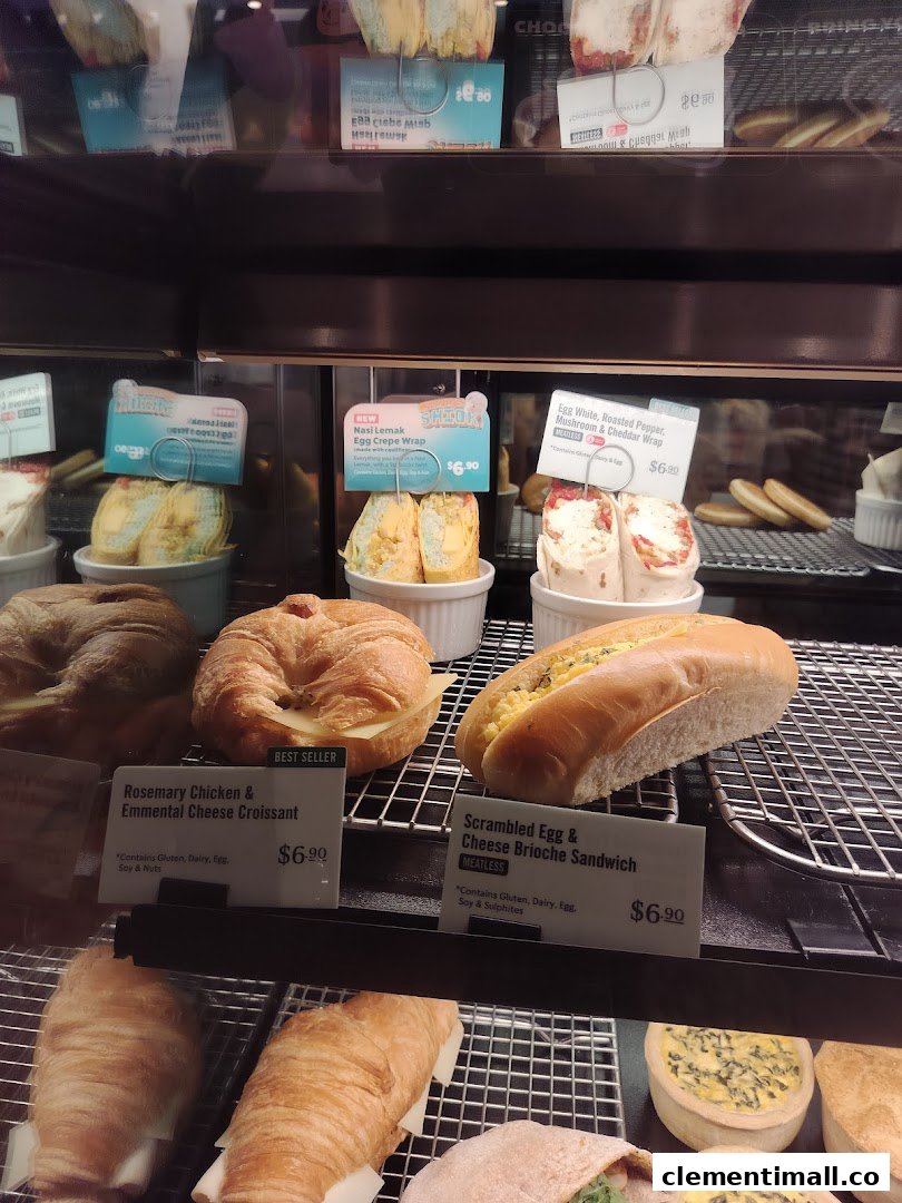 A display case at Starbucks showcasing a variety of fresh pastries, wraps, and sandwiches with prices.