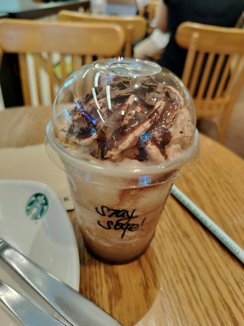 A close-up of a Starbucks Frappuccino with whipped cream and chocolate shavings on a wooden table.
