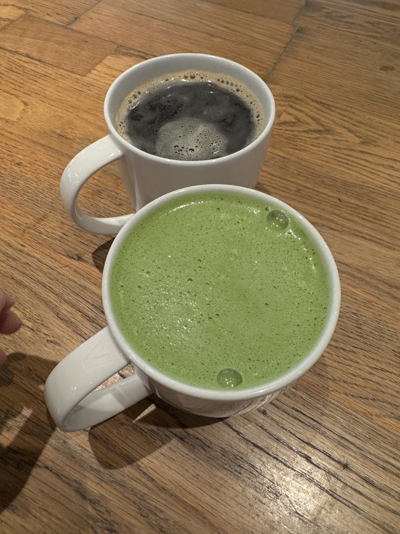 Two beverages, a black coffee and a green matcha latte, on a wooden table.