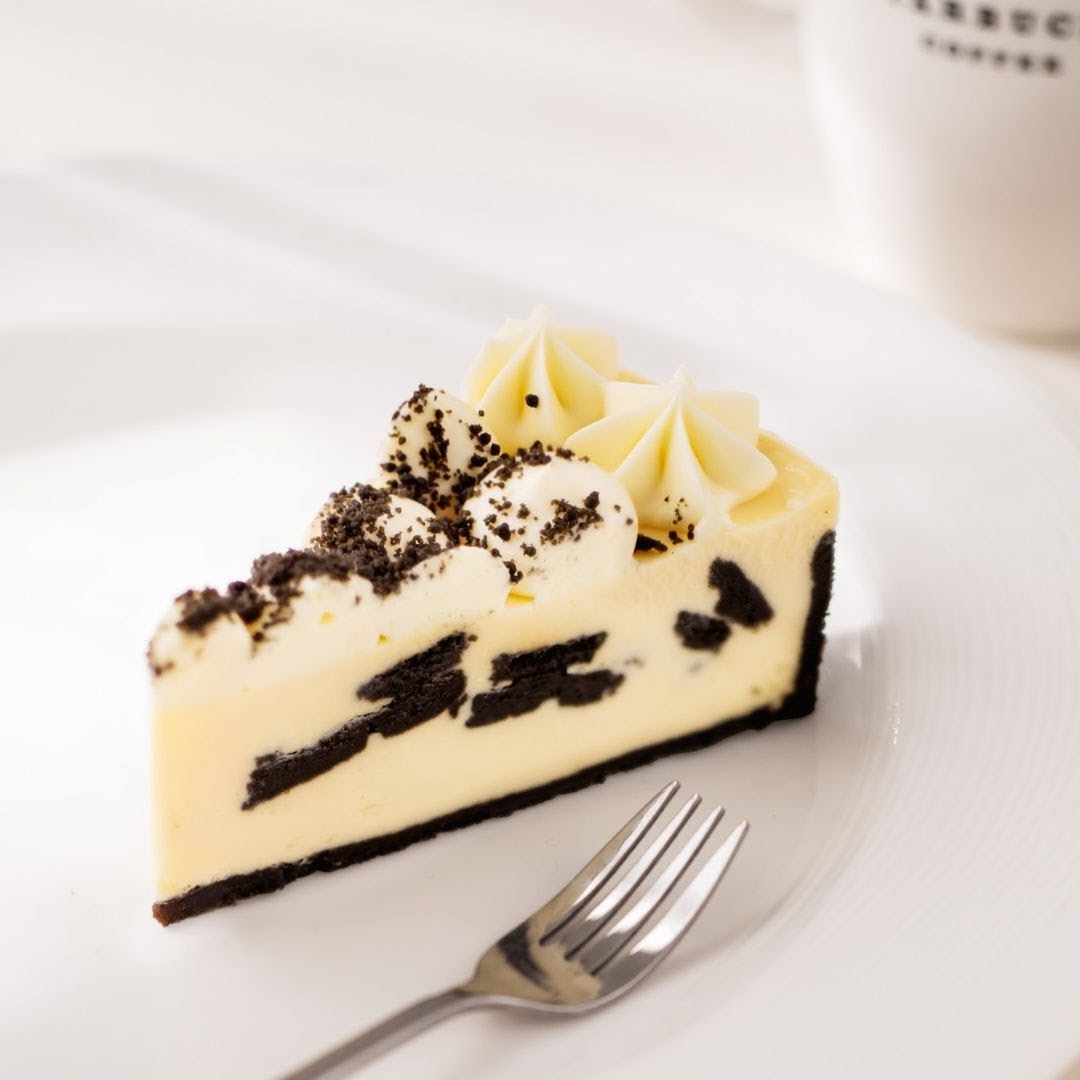 A delicious slice of cookies and cream cheesecake with a fork on a white plate.