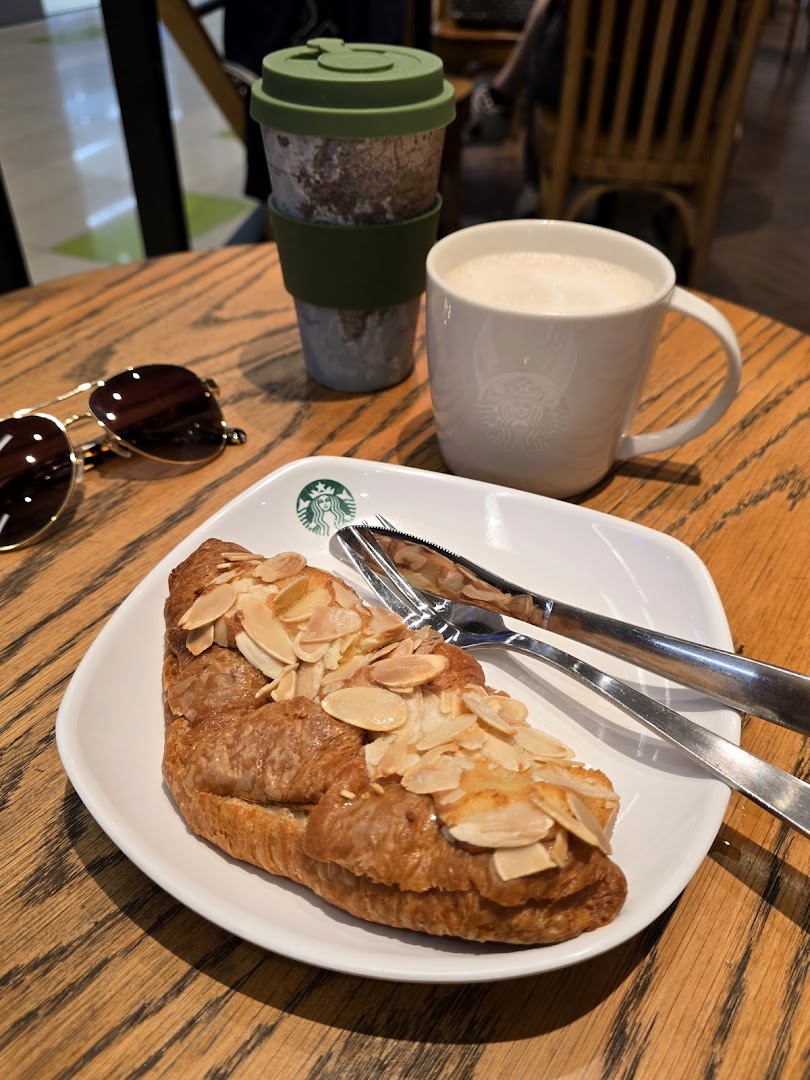 A delicious almond croissant and coffee on a wooden table at Starbucks Clementi Mall.