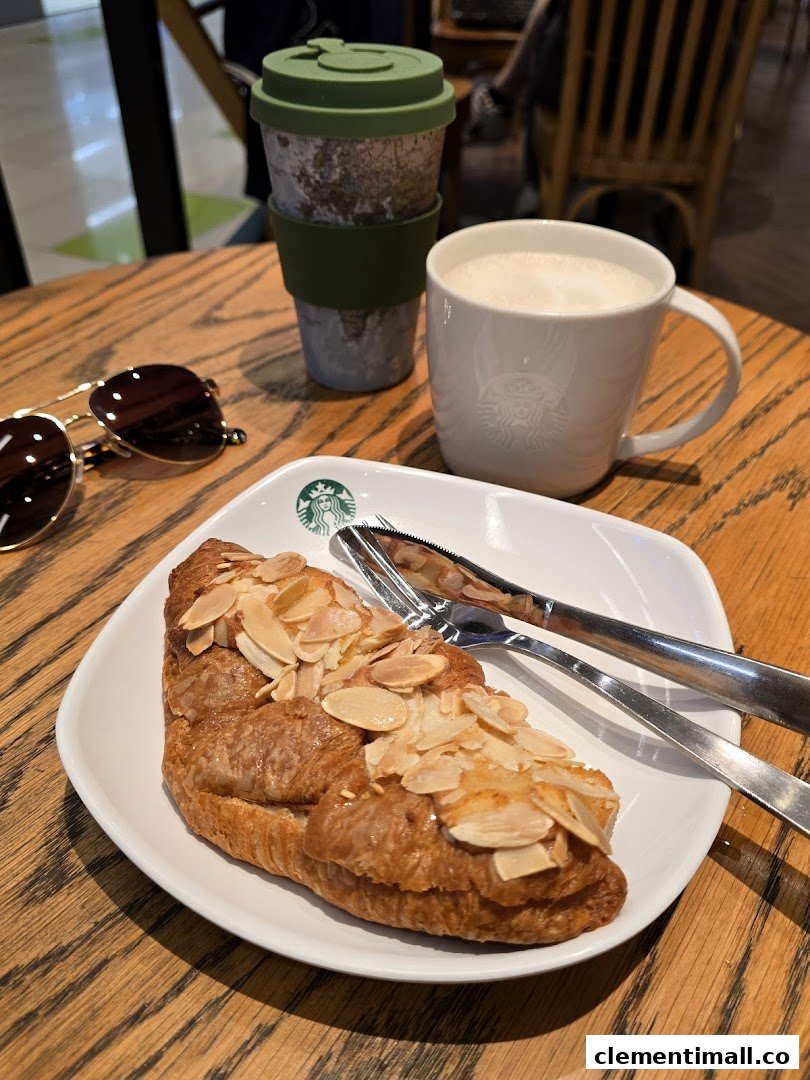 A delicious almond croissant and coffee on a wooden table at Starbucks Clementi Mall.