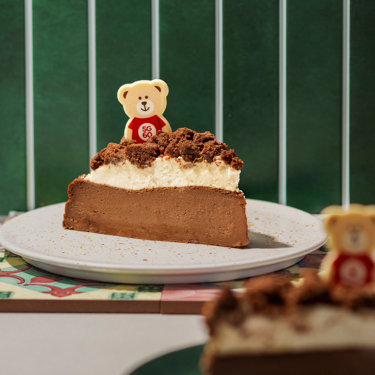 A delicious slice of chocolate and cream cake topped with cookie crumble and a bear-shaped chocolate.