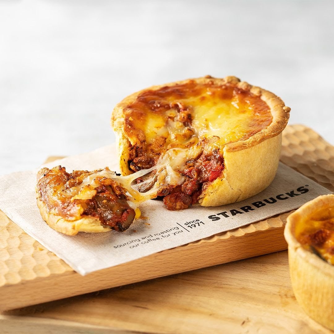 A delicious savory pie with melted cheese and rich filling, served on a wooden board with a Starbucks napkin.
