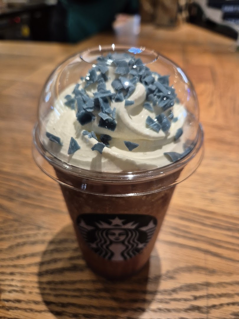 A Starbucks Frappuccino with whipped cream and unique blue toppings on a wooden table.