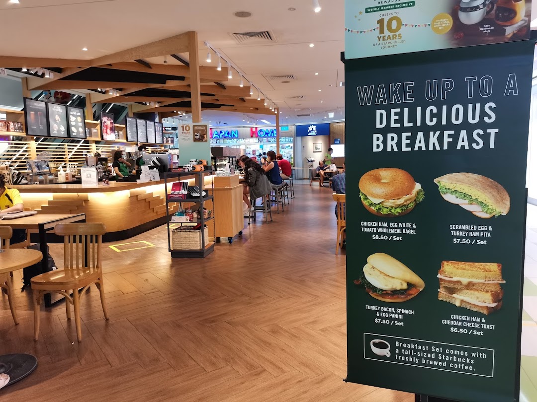 Interior view of Starbucks Clementi Mall, featuring the counter, seating, and a prominent breakfast menu banner.