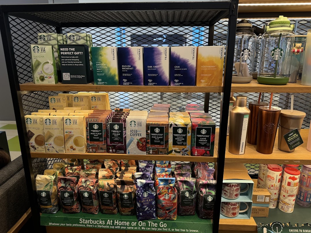 A retail display shelf inside Starbucks, featuring packaged coffee, tea, and branded drinkware.