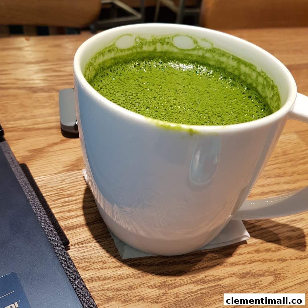A close-up of a frothy green matcha latte in a white mug on a wooden table at Starbucks.