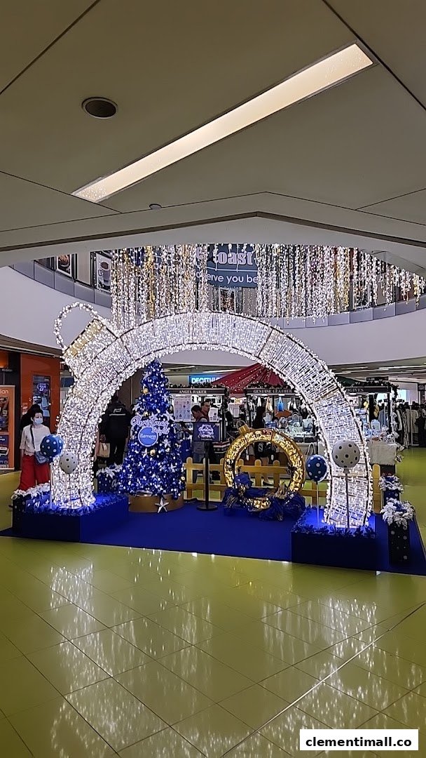 A festive mall interior featuring a large, illuminated Christmas ornament archway and a blue Christmas tree display.