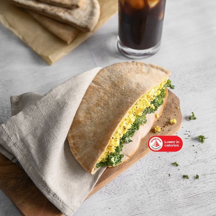 A wholesome pita sandwich filled with scrambled eggs and greens, served with a refreshing iced drink.