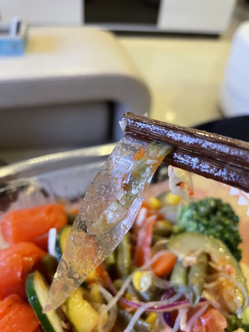 Close-up of fresh ingredients, including vegetables and noodles, held by chopsticks from a Stuffd bowl.