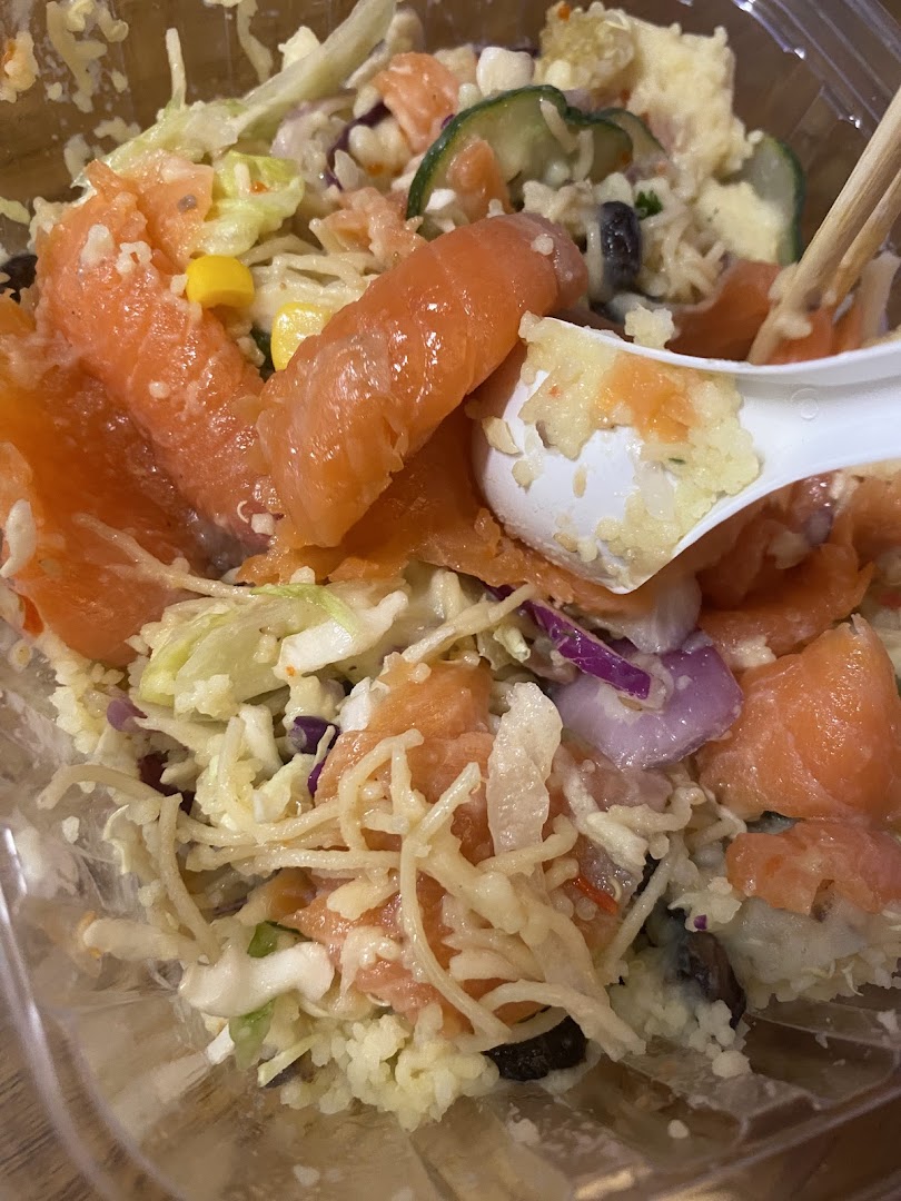 Close-up of a fresh salmon and rice bowl with various vegetables and a spoon.