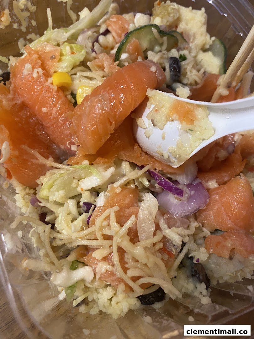 Close-up of a fresh salmon and rice bowl with various vegetables and a spoon.
