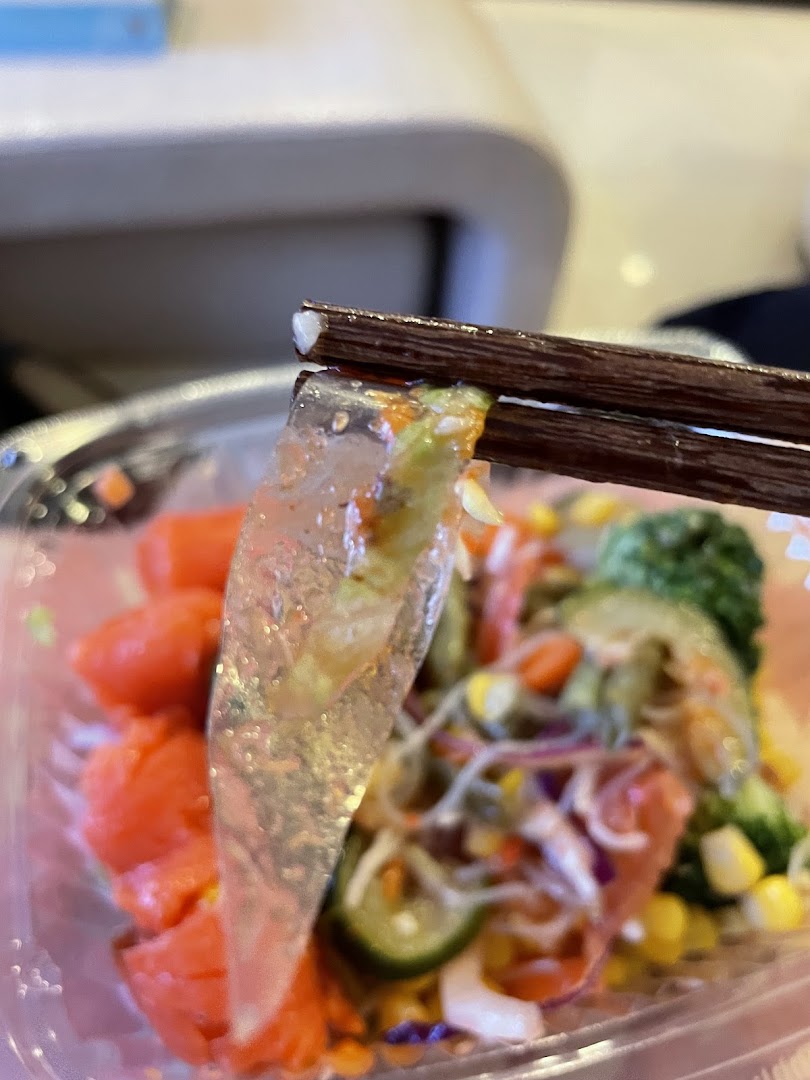 Close-up of a fresh, colorful salad bowl with salmon and vegetables, picked up by chopsticks.