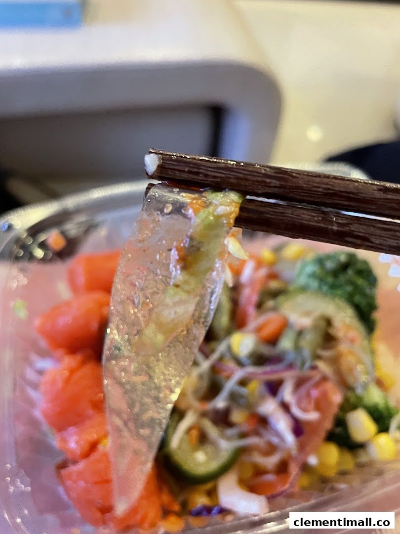 Close-up of a fresh, colorful salad bowl with salmon and vegetables, picked up by chopsticks.