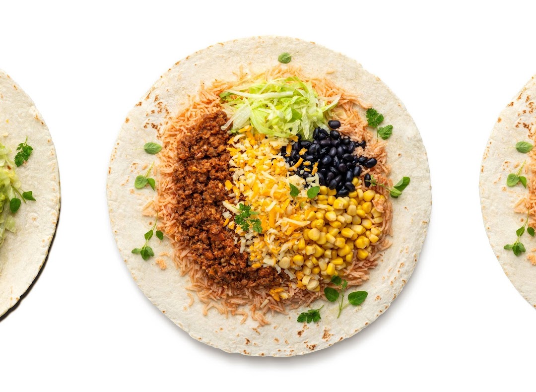 An overhead view of an open wrap filled with rice, ground meat, cheese, corn, black beans, and lettuce.