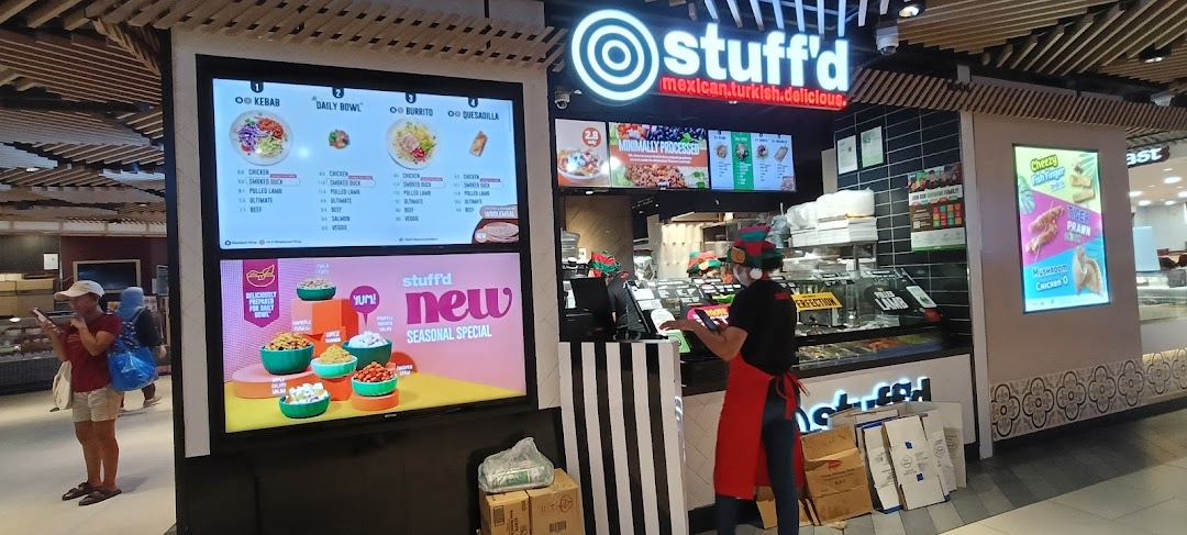 A vibrant Stuffd shop front with digital menu displays and a staff member, showcasing fresh food options.