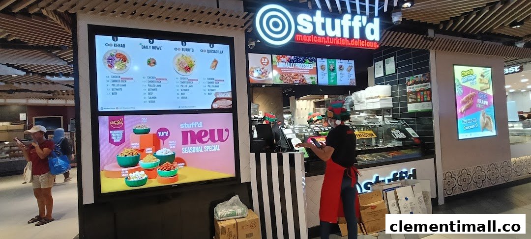 A vibrant Stuffd shop front with digital menu displays and a staff member, showcasing fresh food options.