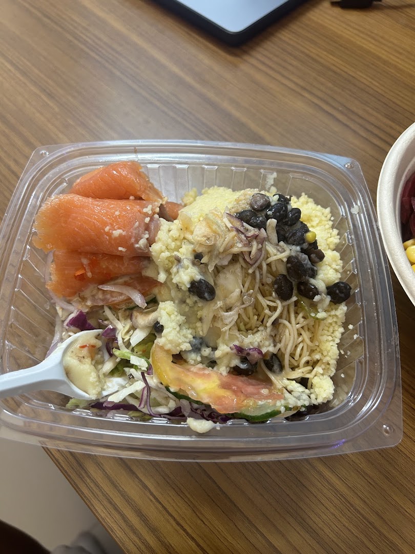 A clear plastic bowl filled with a vibrant, healthy salad featuring salmon, couscous, and mixed vegetables.
