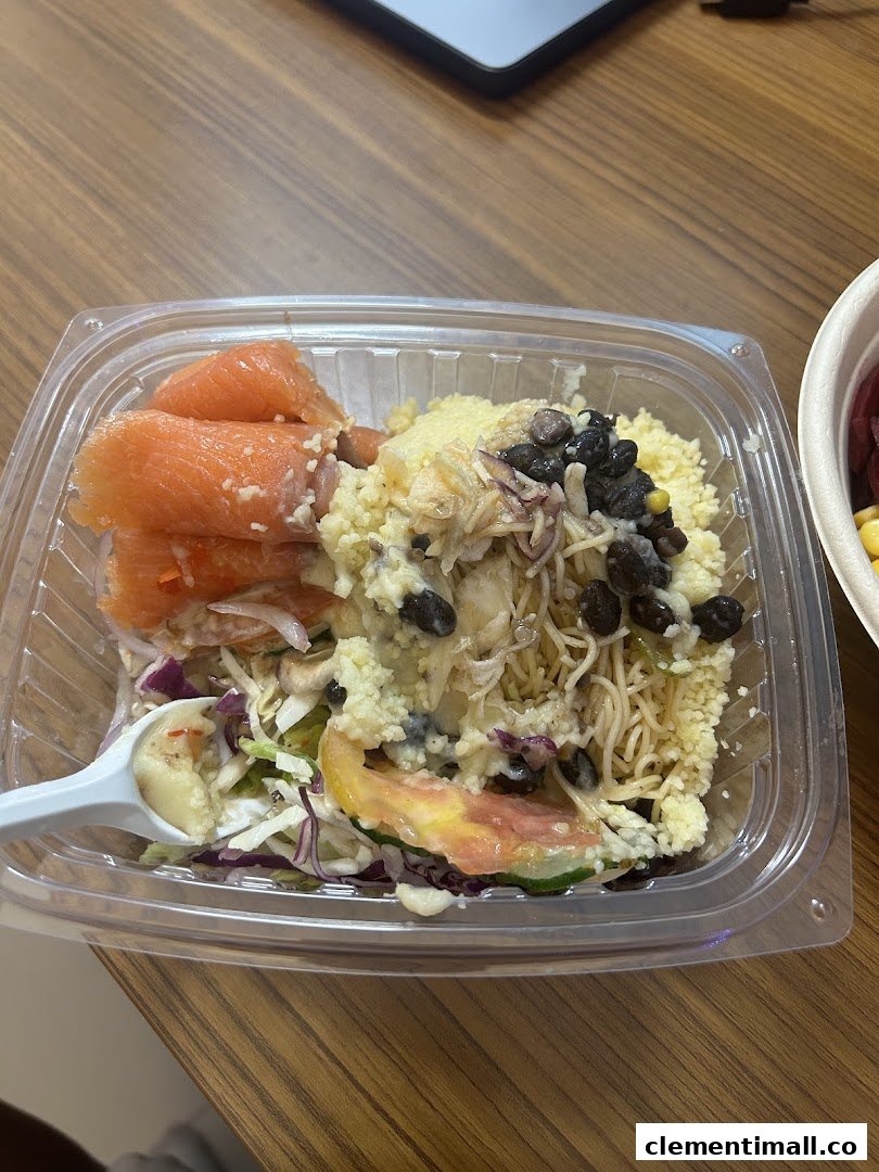 A clear plastic bowl filled with a vibrant, healthy salad featuring salmon, couscous, and mixed vegetables.
