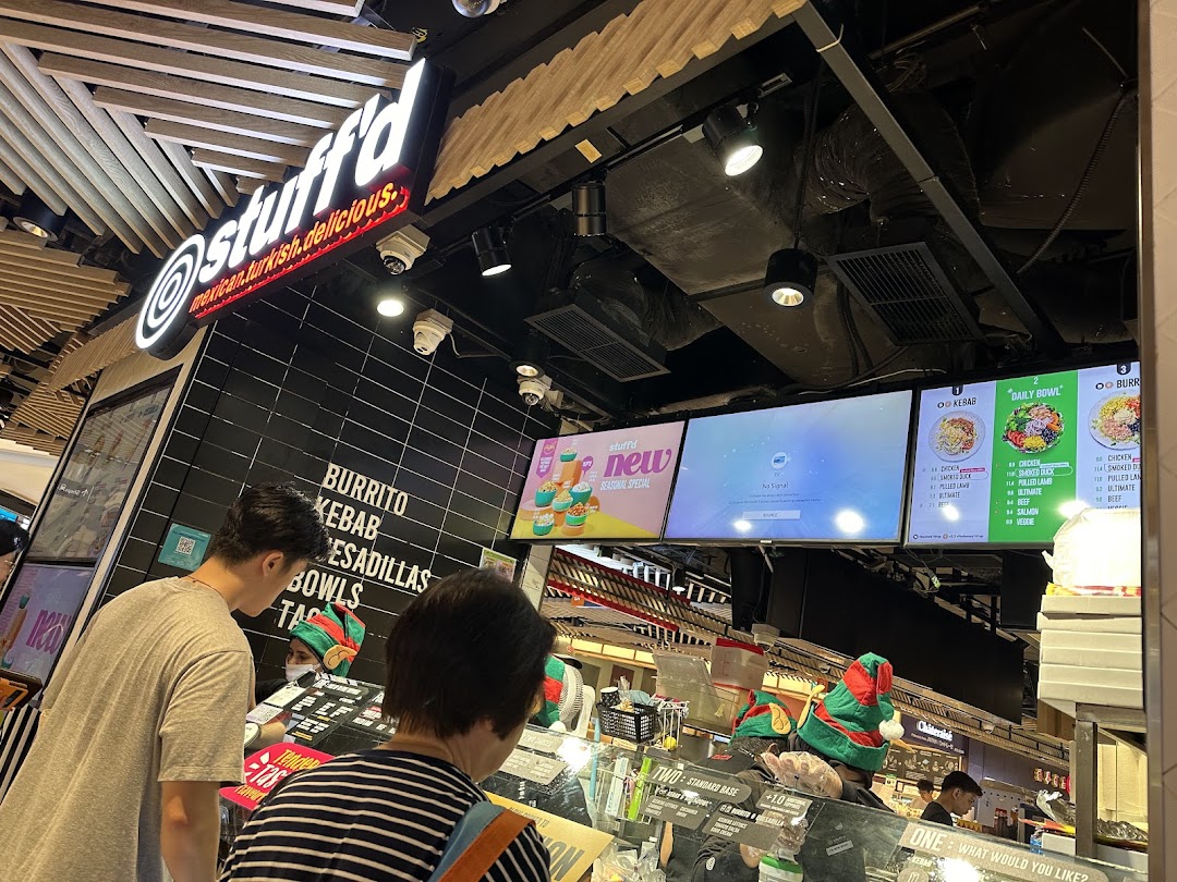 Customers ordering at Stuffd's counter, featuring digital menu boards displaying various food options and prices.