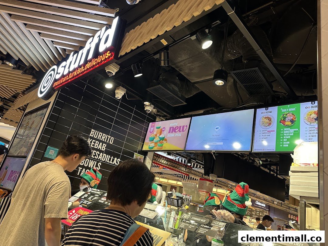 Customers ordering at Stuffd's counter, featuring digital menu boards displaying various food options and prices.
