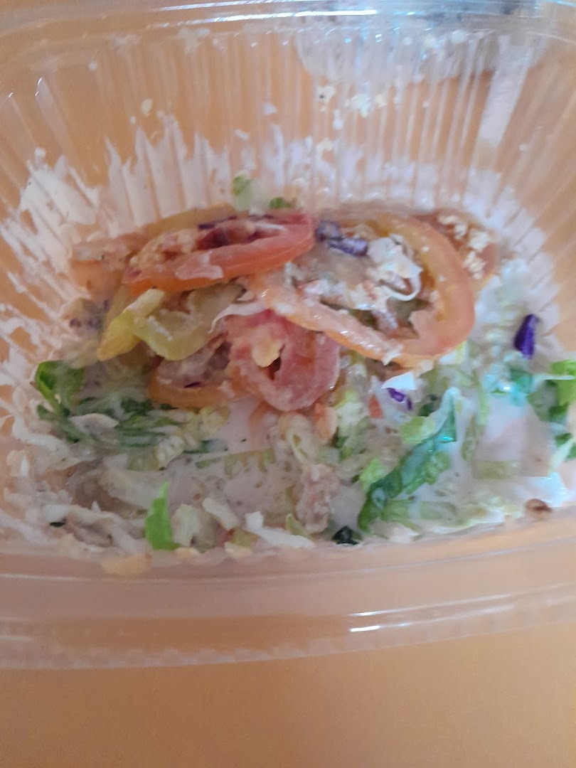 A close-up of a fresh salad with lettuce, tomatoes, and dressing in a clear plastic container.