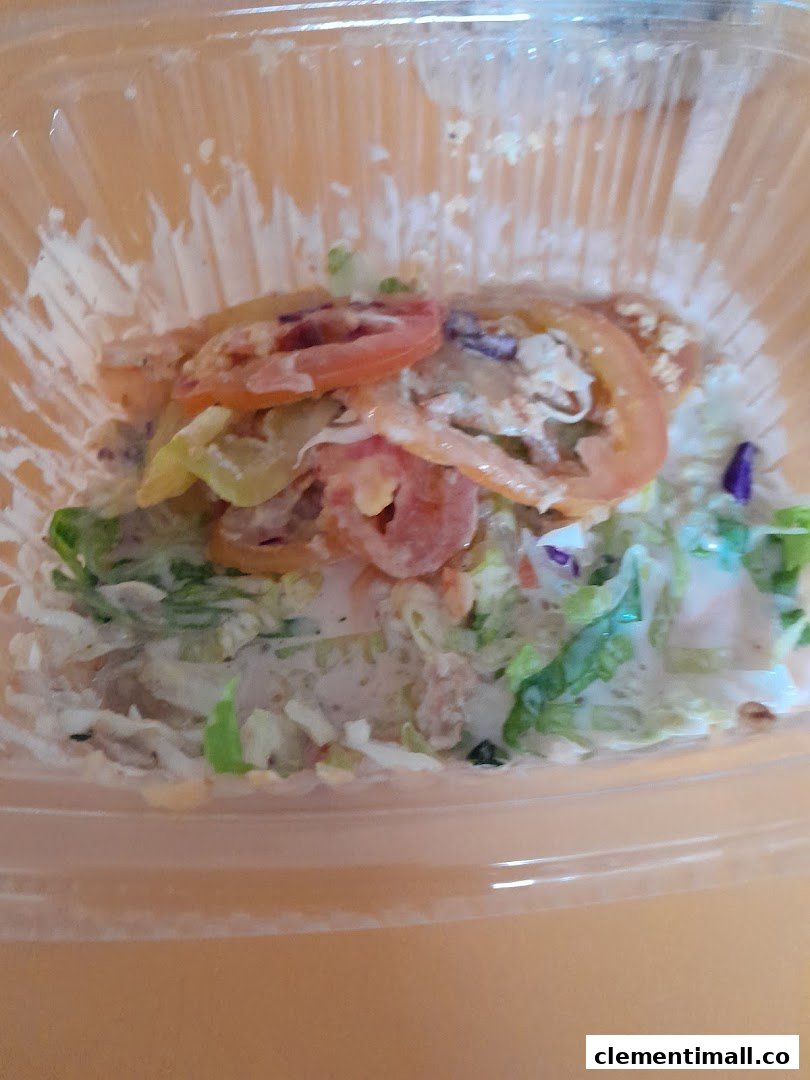 A close-up of a fresh salad with lettuce, tomatoes, and dressing in a clear plastic container.
