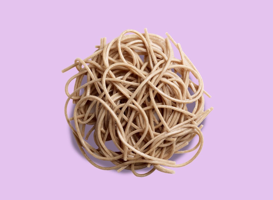 A close-up shot of a tangled pile of cooked noodles on a light purple background.
