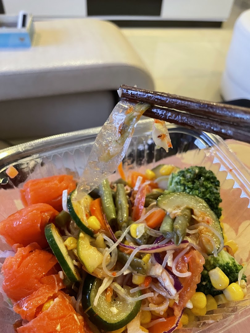 Close-up of a fresh, colorful salad bowl with chopsticks, featuring salmon, noodles, and various vegetables.