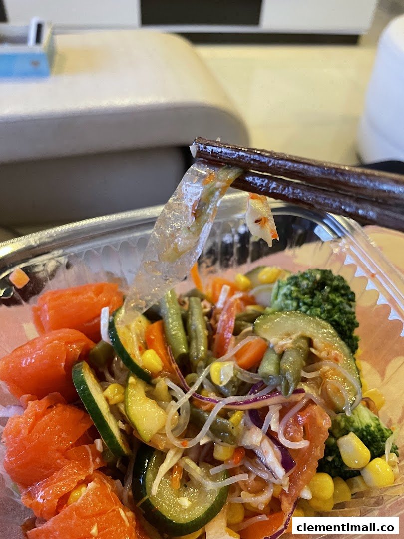 Close-up of a fresh, colorful salad bowl with chopsticks, featuring salmon, noodles, and various vegetables.